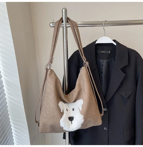 Detail view of a brown canvas bag with a cute white puppy plush patch on a silver hanger