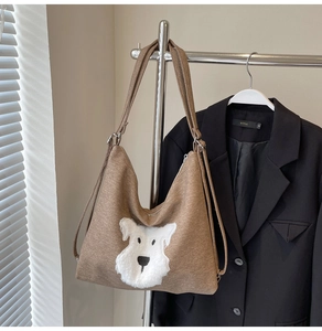 Close-up of brown canvas tote bag with white plush dog patch and metal zipper closure