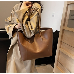 Detail view of brown leather tote bag with white contrast stitching on model