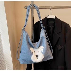 Detail of blue denim tote bag featuring a white plush dog patch on the front pocket