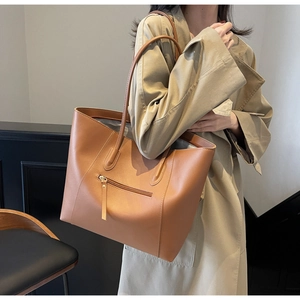 Close-up of a tan tote bag with a gold zipper pocket and smooth leather texture