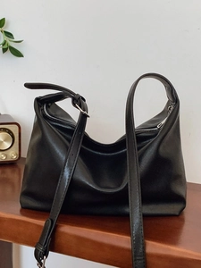 Minimalist black faux leather tote bag with adjustable strap on a wooden tabletop