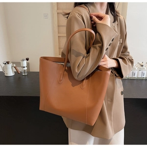 Brown large-capacity leather tote bag shown in a lifestyle setting with a shoulder strap