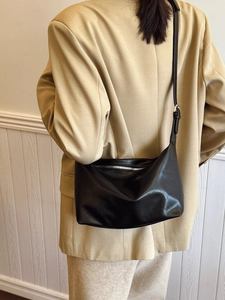 Minimalist black faux leather tote bag with adjustable strap worn by model in a suit