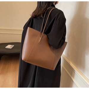 Detail of a large brown leather tote bag with contrast stitching and slim shoulder straps