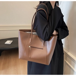 Detail of a large brown leather tote bag with a front zipper pocket worn by a model