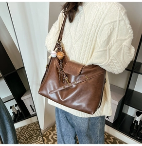 Close-up of vintage brown leather tote bag with engraved flap and baseball charm detail