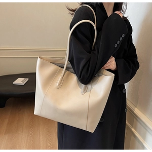 Detail view of large beige leather tote bag on shoulder over black wool coat