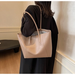 Detail view of the beige minimalist leather tote bag worn as an underarm shoulder bag