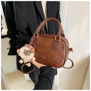Close-up of brown retro leather handbag with geometric stitching and plush sheep charm