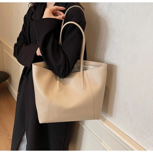 Detail view of large apricot tote bag worn on shoulder over a black outfit for work