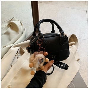 Close-up of black leather crossbody bag with stitching details and a plush bunny charm