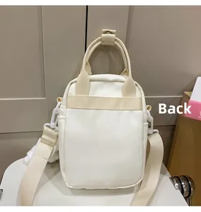 Back view of a minimalist cream canvas crossbody bag with adjustable wide strap and plush charm