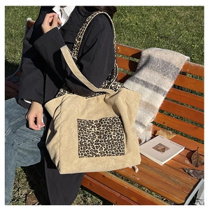 Detail of a leopard print pocket on a beige corduroy tote bag in a casual outdoor setting