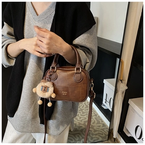 Detail of dark brown leather handbag with gold logo, round handle and lion plush charm