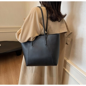 Minimalist matte black tote bag with long straps worn by a model in a French style interior