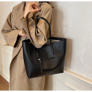 Detail of a large black leather tote bag featuring a front zipper pocket and long straps