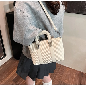 Close-up of beige textured tote bag featuring silver metal buckles and detachable strap