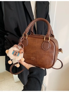 Brown leather mini crossbody bag with plush bear charm shown in a side-view model shot
