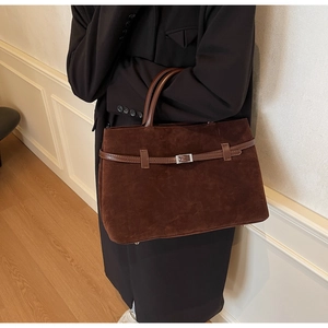 Close-up of matte brown suede tote bag with silver buckle and metal feet on the bottom