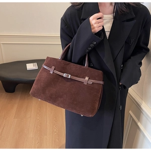 Detail of dark brown suede tote bag featuring rounded handles and decorative buckled straps