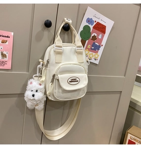 Detail of cream canvas bag featuring brand logo and cute white puppy plush charm