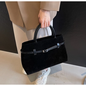 Close-up of black matte suede tote bag with decorative metal buckle and dual handles