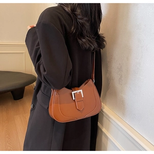 Detail of caramel brown saddle bag with large silver buckle worn by a female model