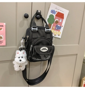 Detail of black nylon crossbody bag with cute plush puppy charm and clear pocket