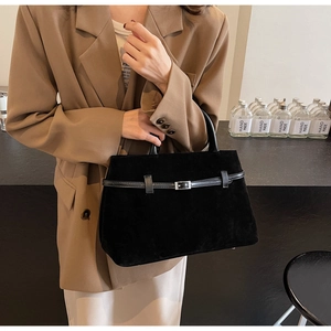 Detail of black suede tote bag with leather strap and silver buckle held by a model