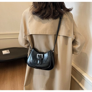 Detail of a black half-moon crossbody bag with silver buckle on a khaki trench coat