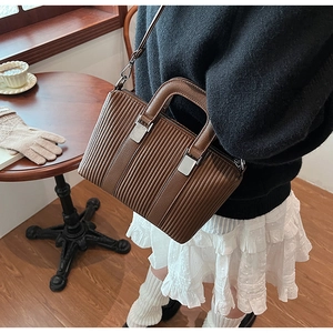 Detail of a brown pleated crossbody bucket bag featuring a unique vertical wavy texture