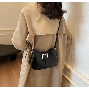 Close-up of black glossy shoulder bag with oversized silver buckle on trench coat
