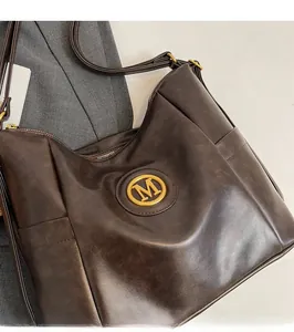 Detail of soft brown PU leather tote showing the gold M logo and smooth zipper closure