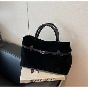 Close-up of matte black suede tote bag featuring leather straps and metal buckle detail