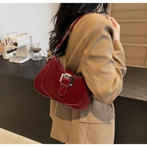 Model wearing a burgundy underarm bag with silver buckle in a cozy cafe setting