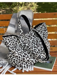 Leopard print canvas tote bag with black handles on a wooden bench with accessories