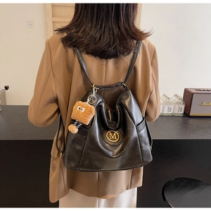 Detail of a large black leather backpack with a gold M logo and a cute bear charm