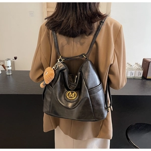 Detail view of a black faux leather backpack with gold M logo and brown plush bear charm