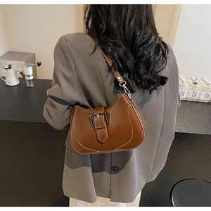 Detail of a brown glossy leather shoulder bag with silver buckle worn on a model