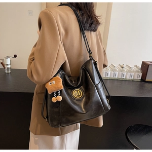 Close-up of black leather tote bag with metallic M logo and cute plush cookie charm
