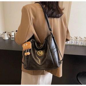 Detail view of large black leather tote with golden M logo and fuzzy monster charm