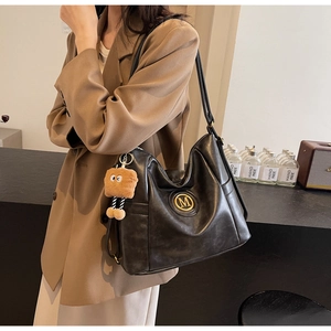 Close-up of black hobo bag with M-logo, leather texture and cute brown bear charm