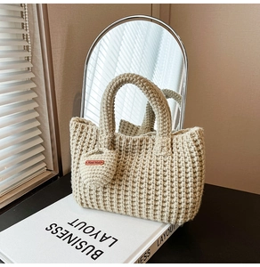 Detail of hand-knitted beige bucket bag with 'Hand Made' heart charm and woven texture