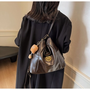 Detail of dark brown leather hobo bag with gold M logo and cute bear charm on shoulder