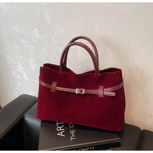 Close-up of matte velvet texture and decorative buckle belt on a burgundy tote bag