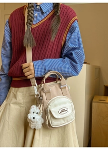 Detail showing beige canvas crossbody bag with plush puppy charm and brand logo
