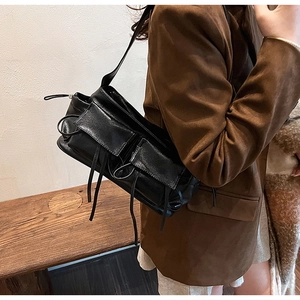 Detail of black faux leather baguette bag with decorative long tassel and double pockets
