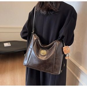 Detail of dark brown leather tote bag featuring a gold M emblem and plush bear charm