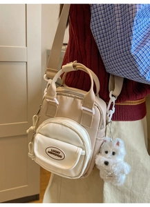 Detail of beige canvas crossbody bag with round pocket and plush dog keychain accessory
